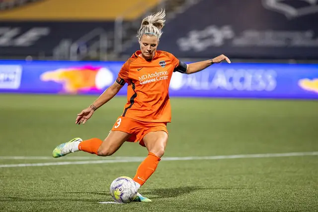 A female soccer player kicking the ball on a field.